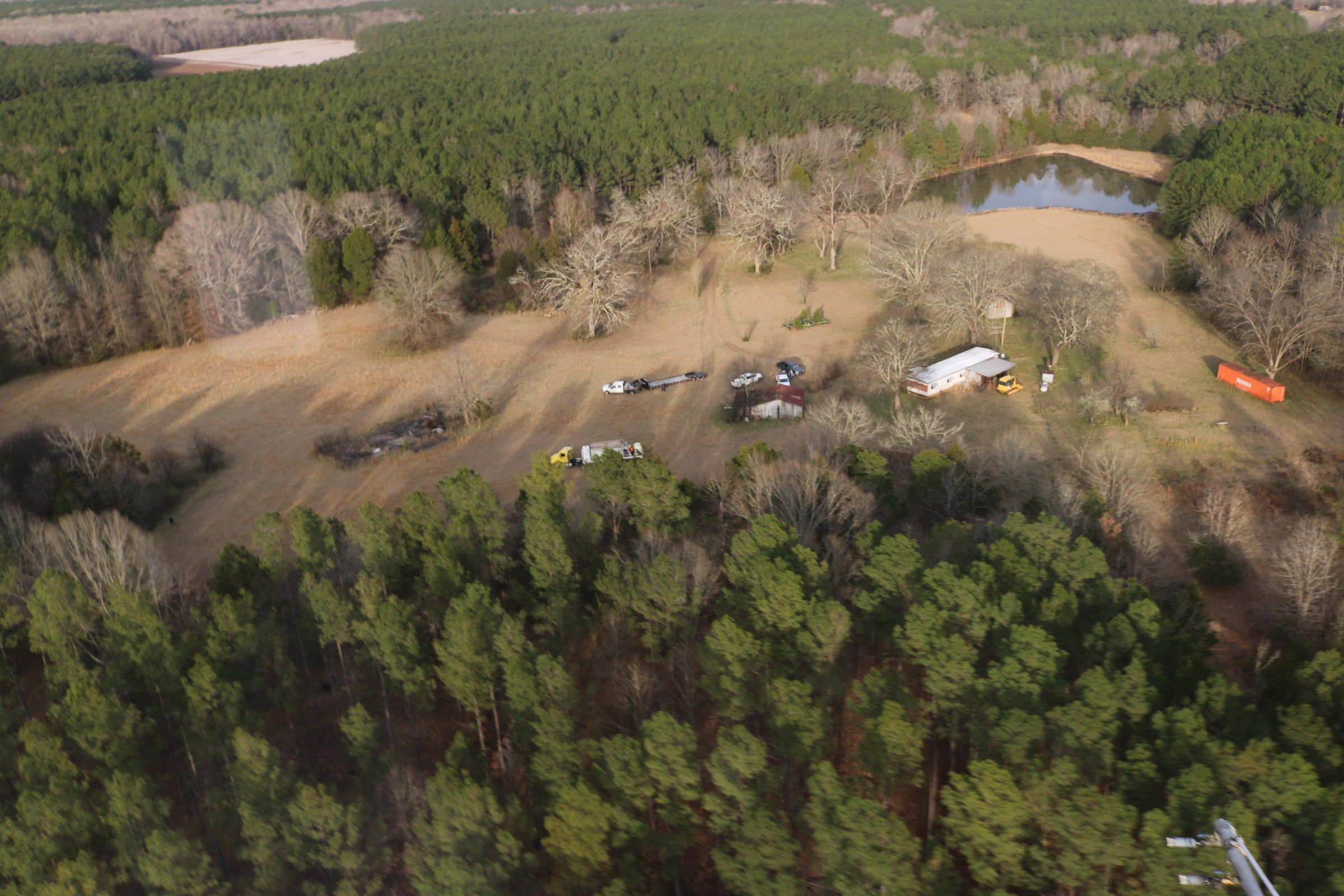 A staging area from the air — nurse truck, mix tank and crew trucks parked in a field at the edge of a pine stand