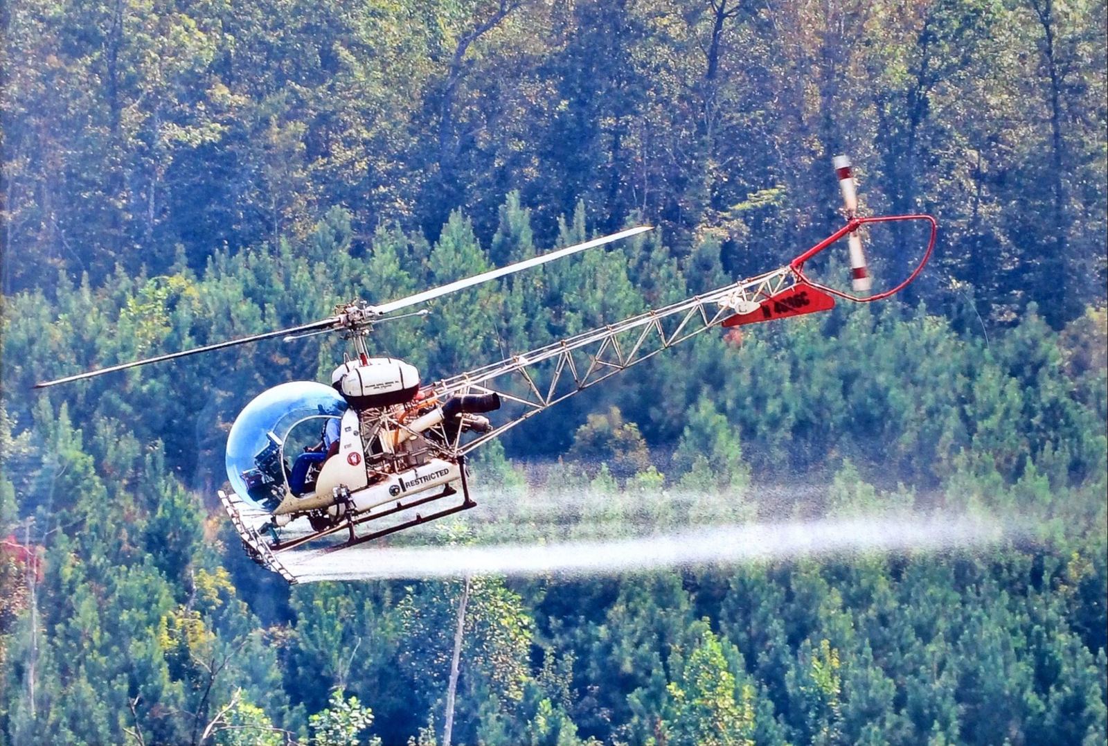 Helicopter releasing a swath of herbicide spray low over Mississippi timberland
