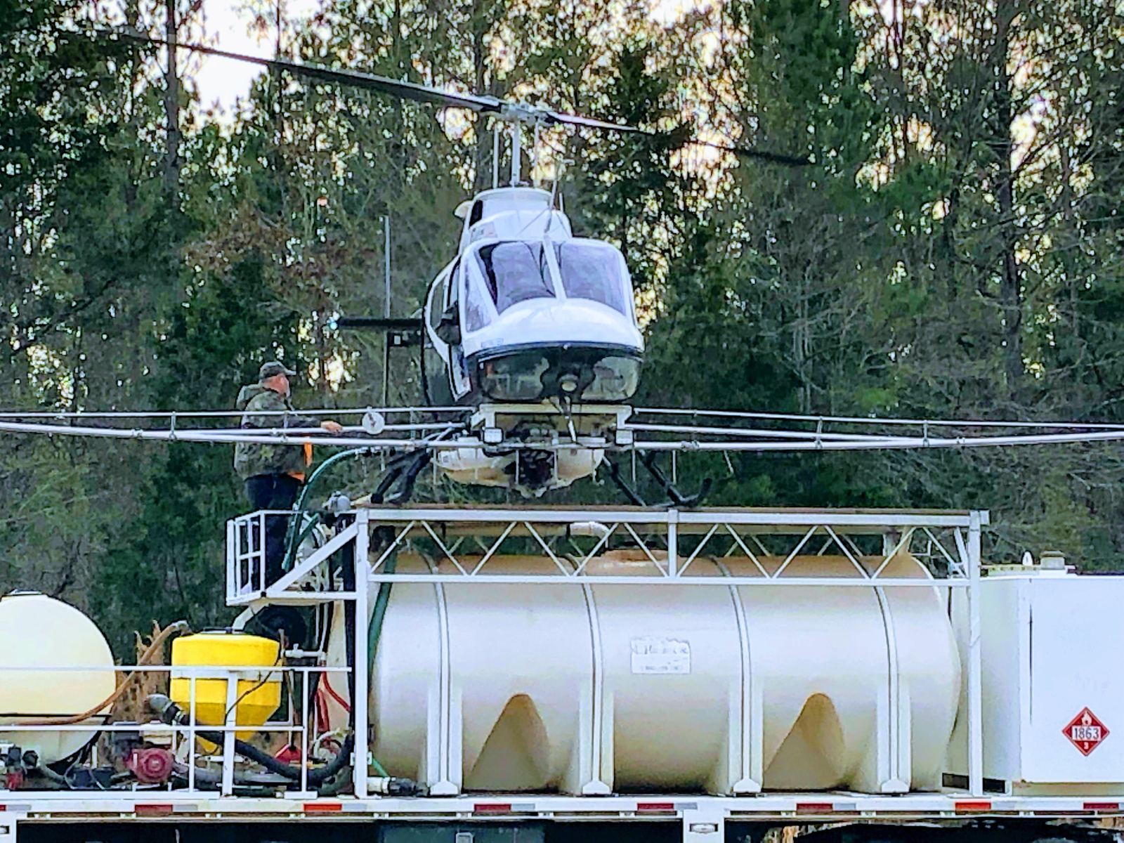 Helicopter set down on the nurse truck's mix tank at the staging site while a crew member loads herbicide
